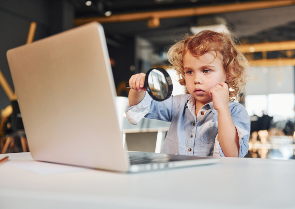 child looking at a laptop with magnification glass